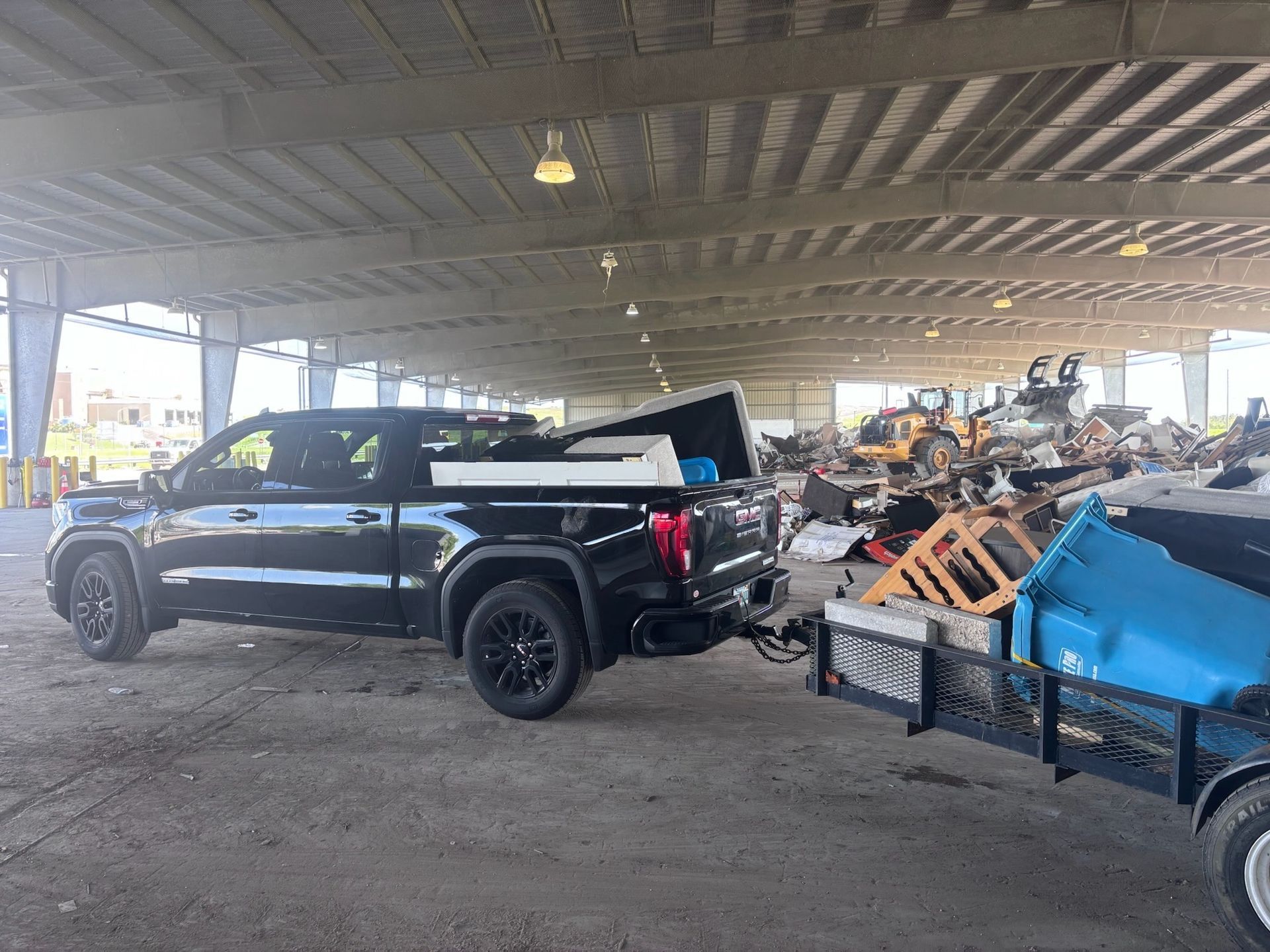 Black pickup truck towing trailer loaded with items at a waste disposal facility.