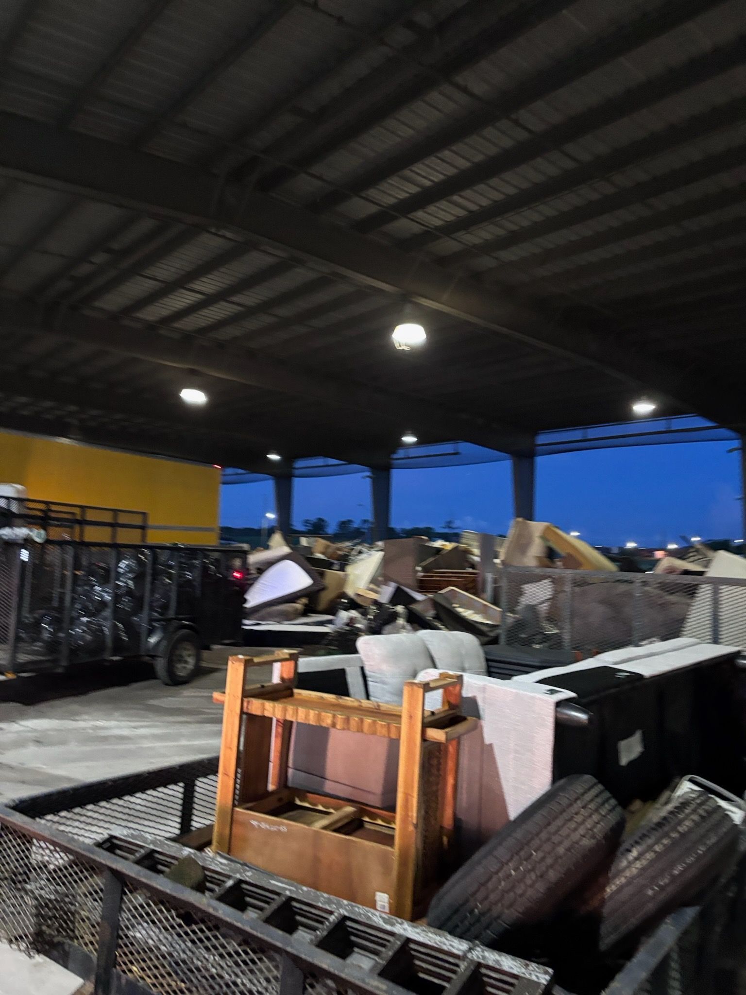 Dump site with piles of discarded furniture and tires under a covered structure.
