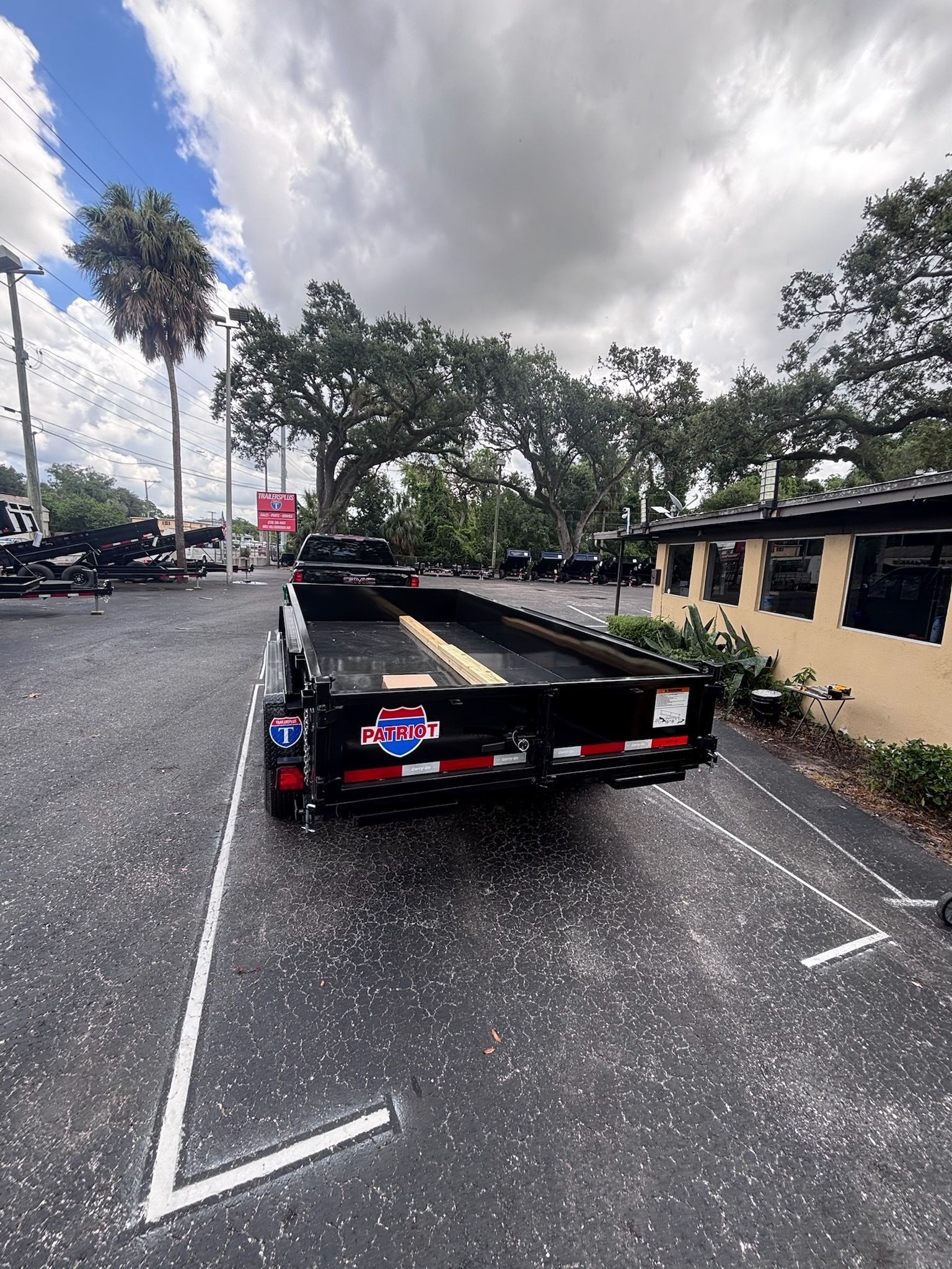 Black trailer parked in a parking space, with a cloudy sky and trees in the background.