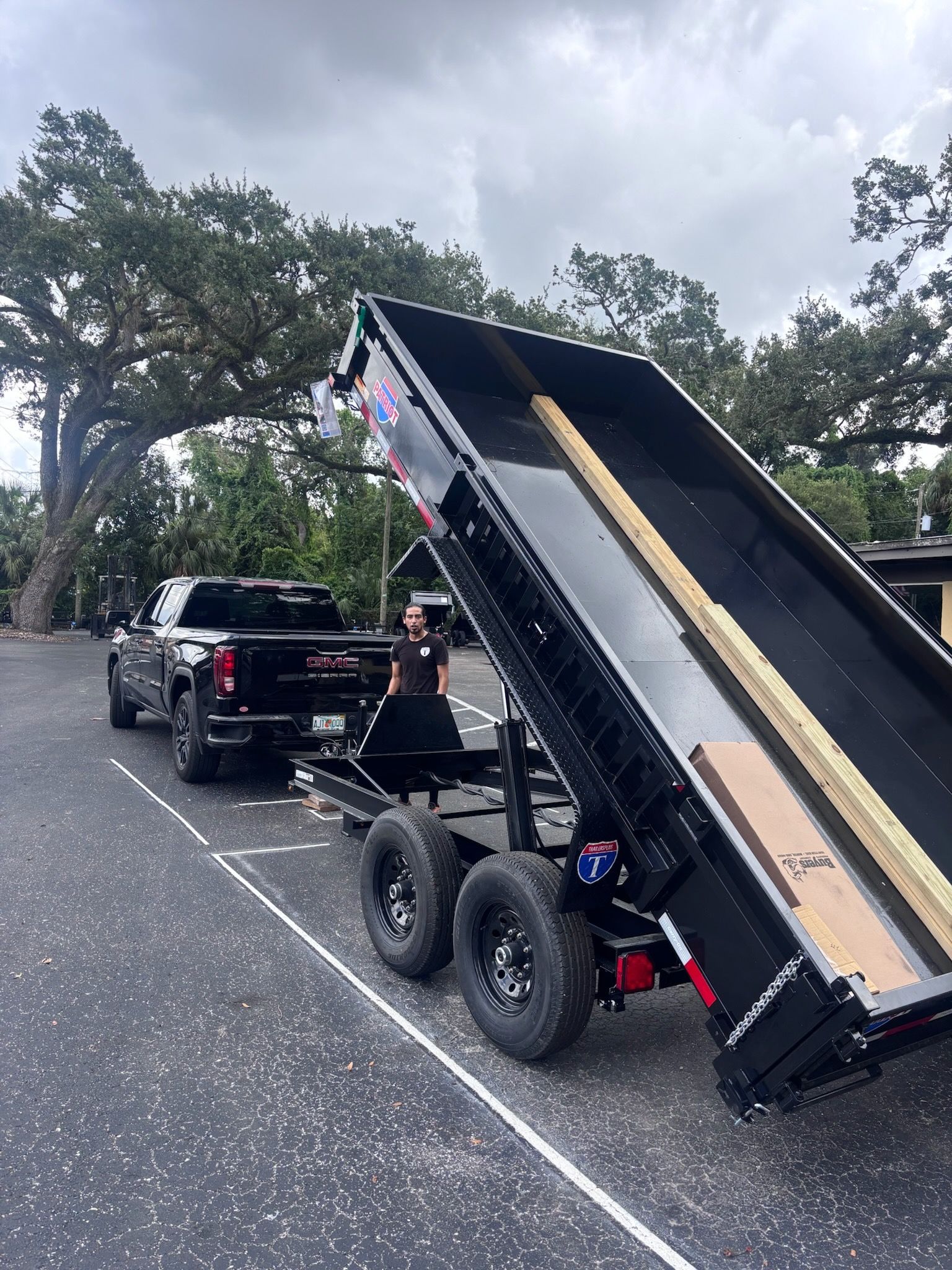 Black truck towing a black dump trailer in a parking lot, trailer bed raised.