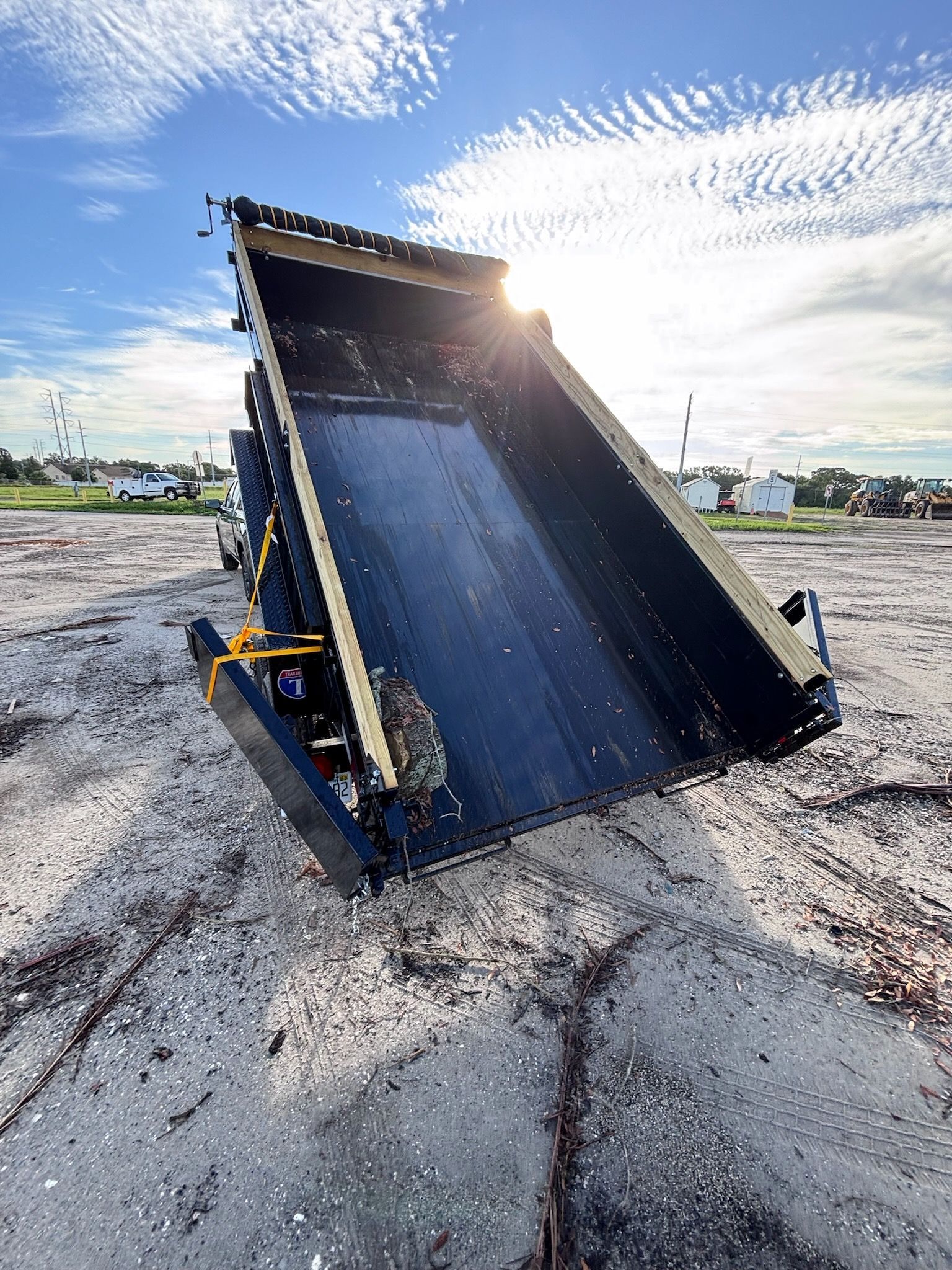 Dump truck bed tilted upwards against a bright blue sky, sunlight beaming.