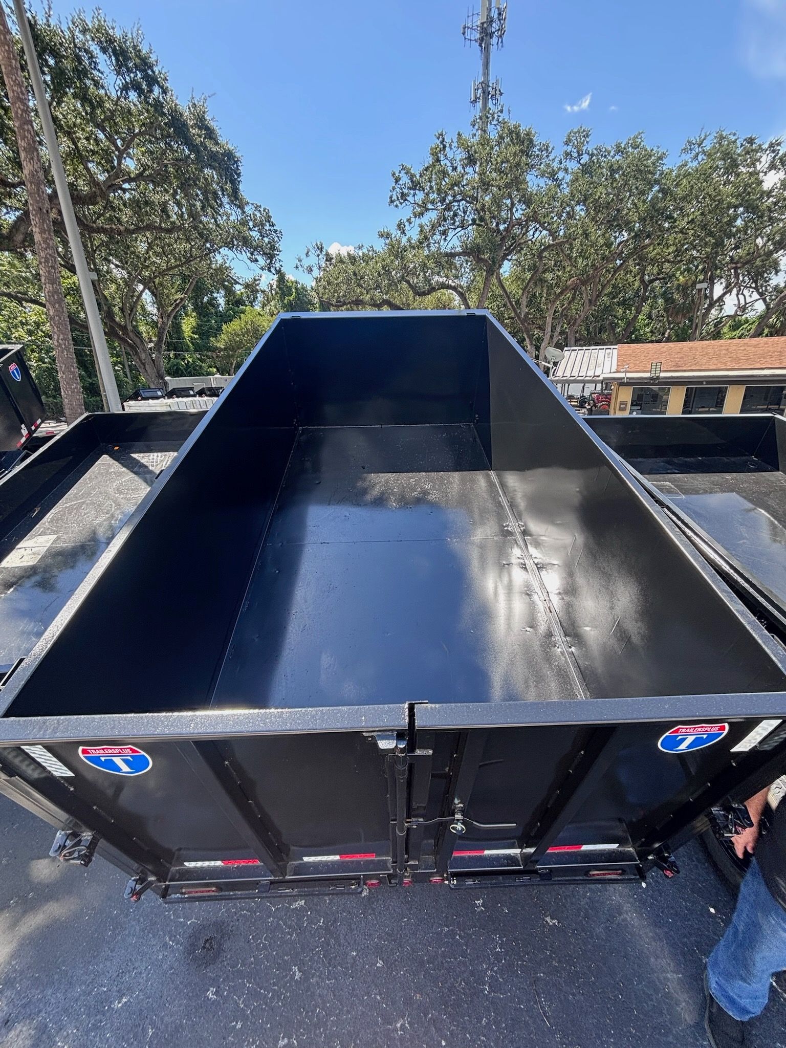 Black dump trailer, empty, outdoors. Metal frame, two doors.