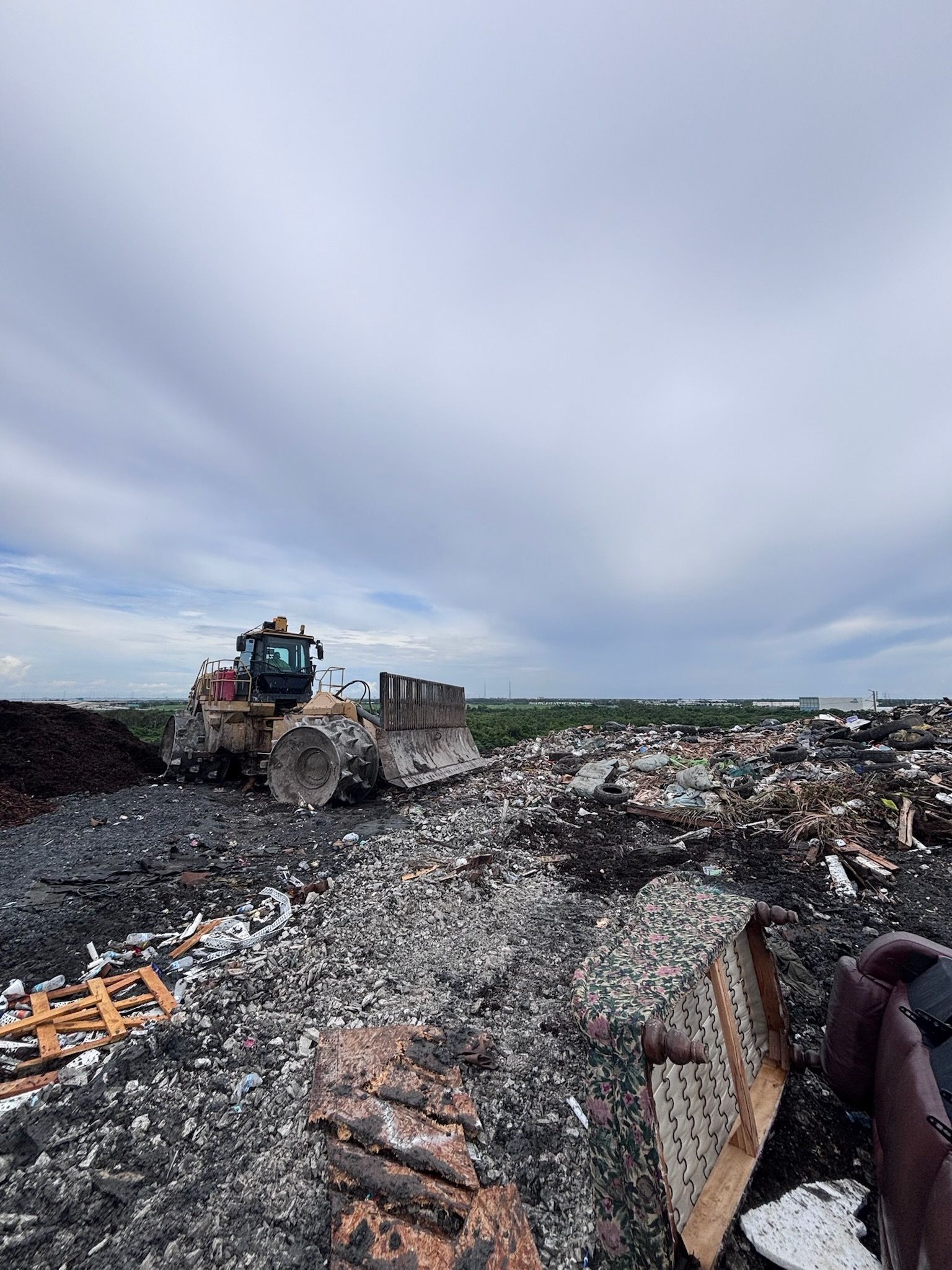 Bulldozer pushing debris at a landfill under a cloudy sky.