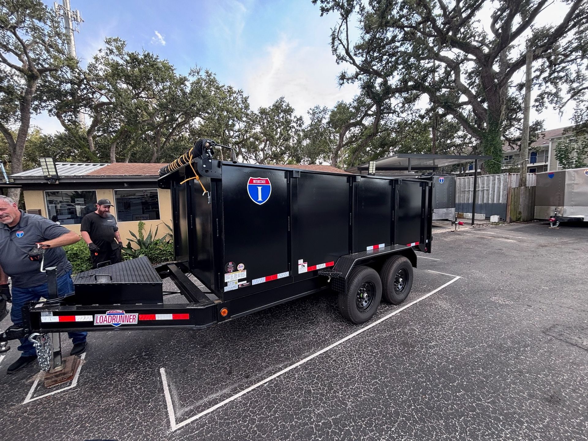 Black dumpster trailer parked in a lot, with two men standing nearby.