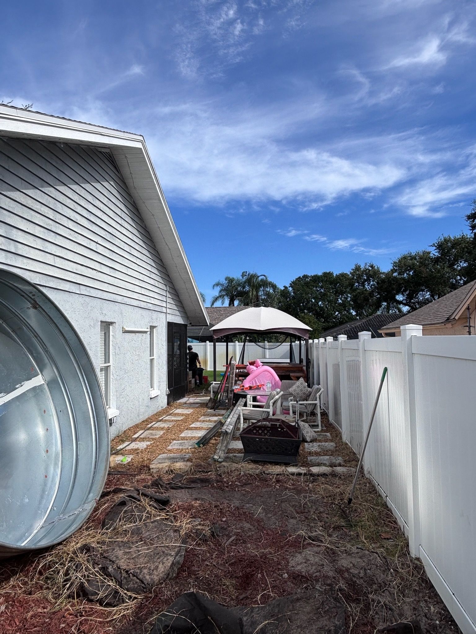Backyard with white fence, gazebo, and house. Blue sky with clouds.