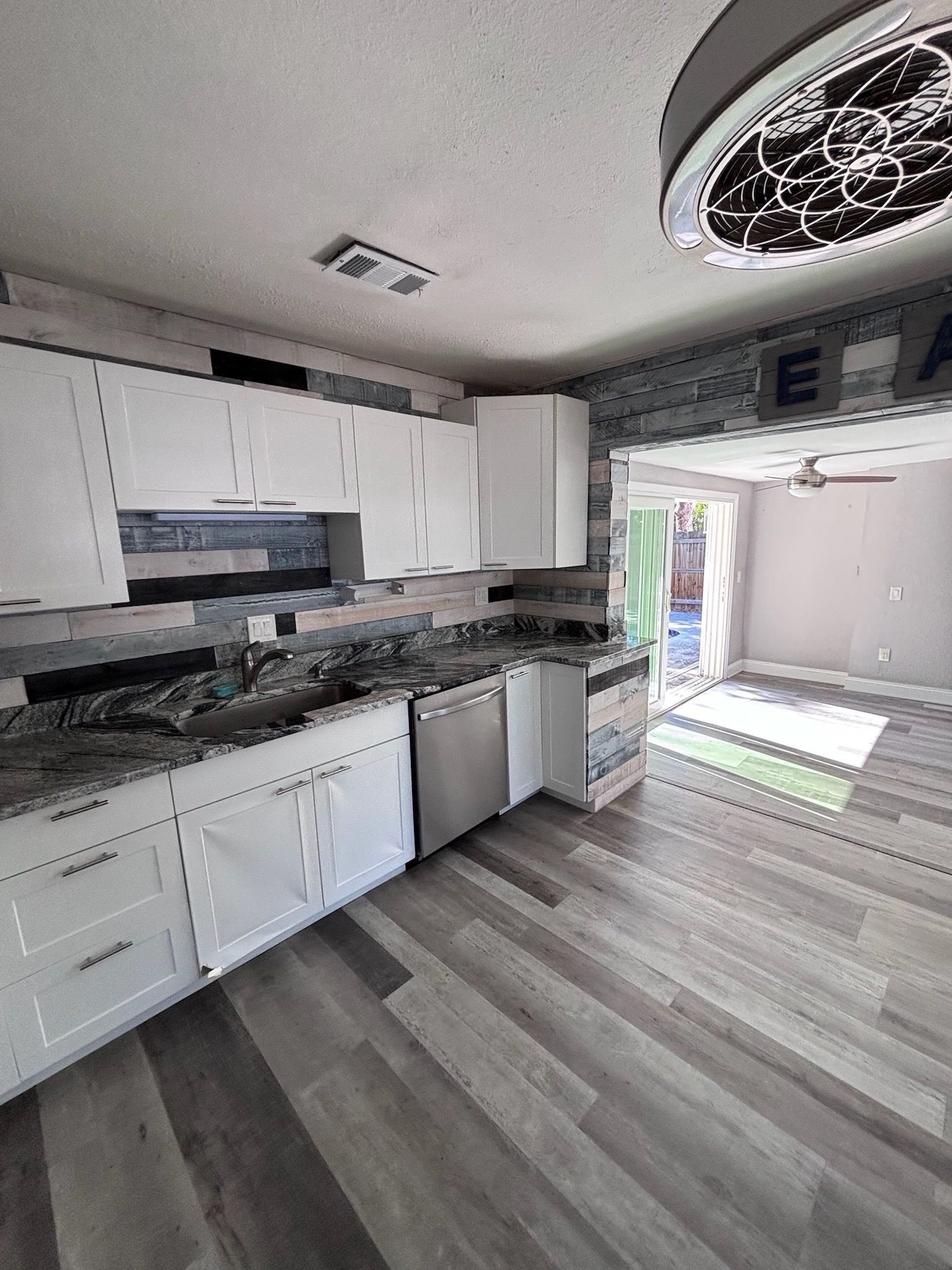 Modern kitchen with white cabinets, gray countertops, and wood-look flooring. Leads to an open living area.