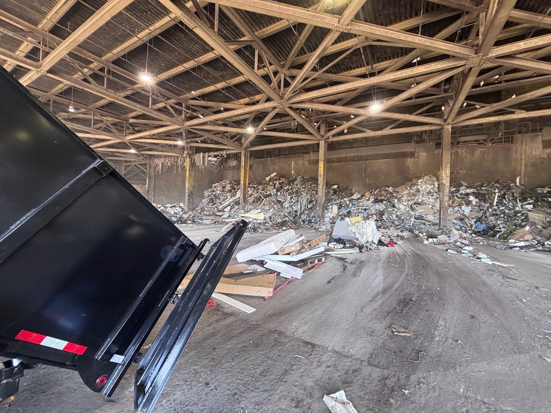 A black dump truck unloading debris into a large indoor recycling facility.