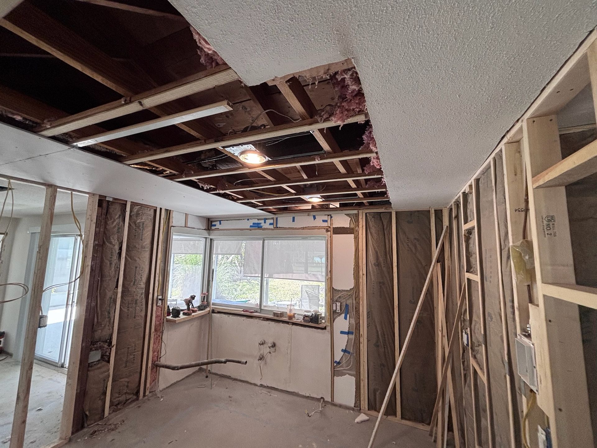 Interior room under construction, exposed wooden framing, insulation, exposed ceiling joists, and a partial ceiling in place.