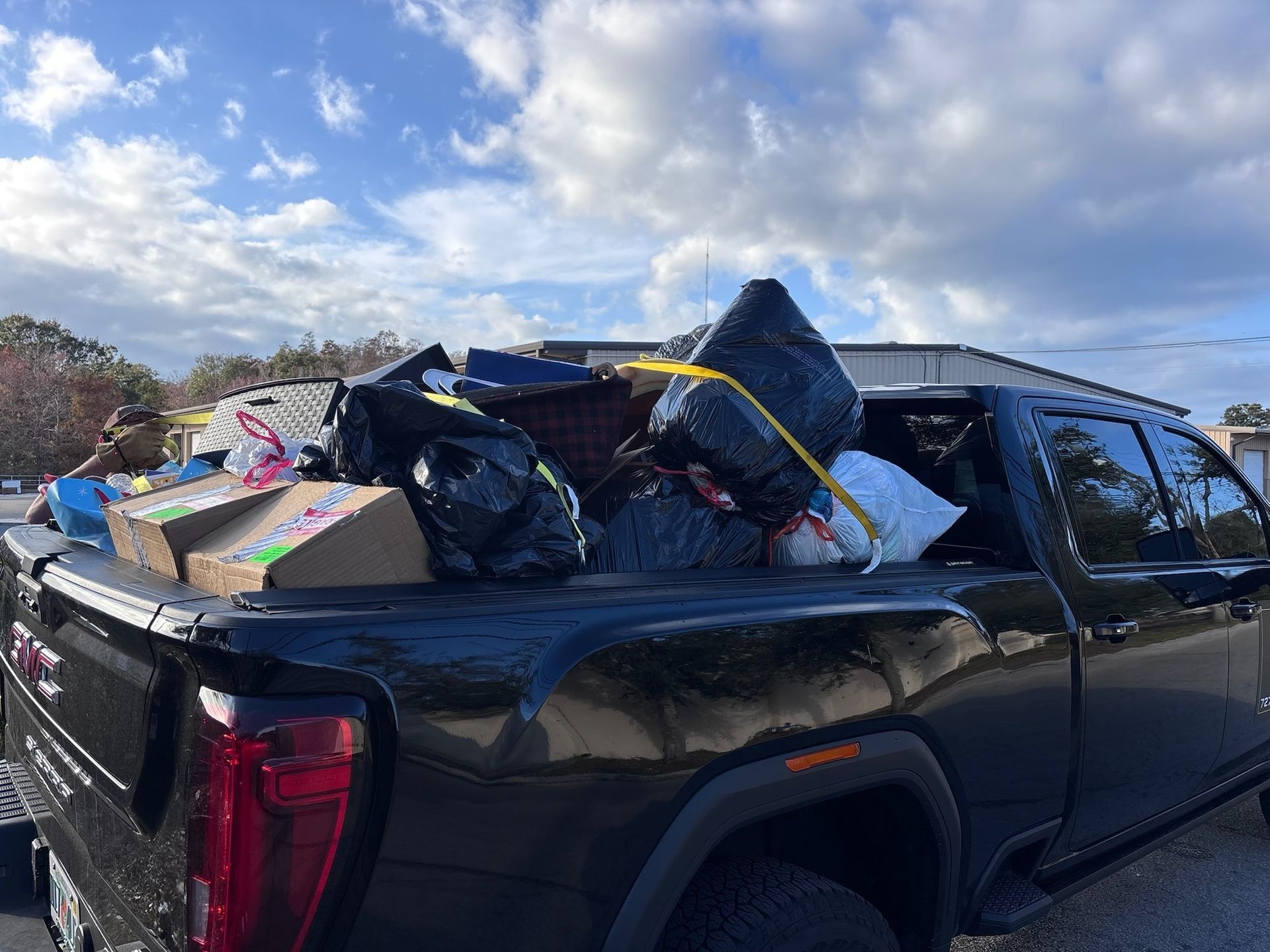 Black pickup truck bed overflowing with trash bags, boxes, and other items under a cloudy sky.