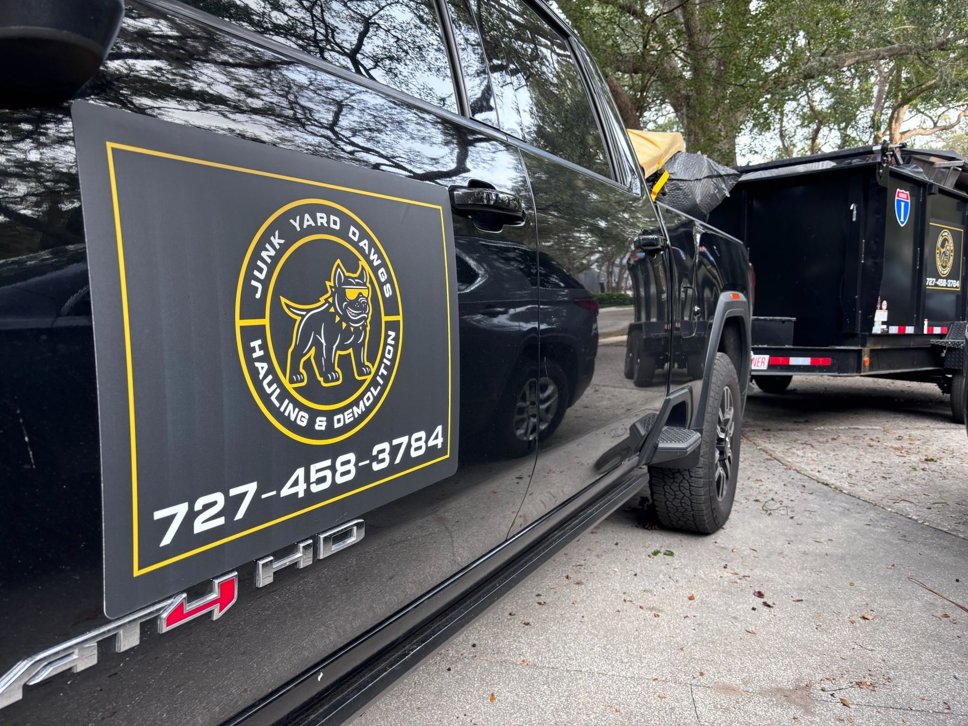 Black truck with magnetic sign for junk removal services; a trailer with a dumpster attached.