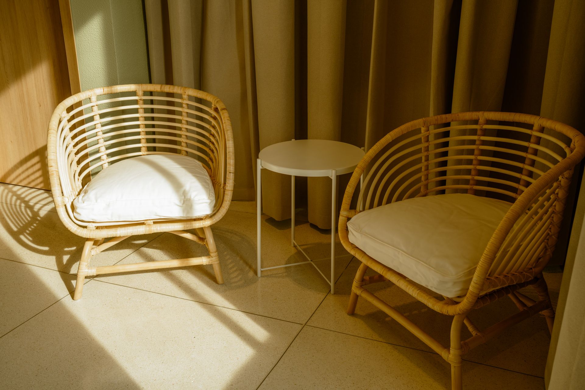 Dos sillas de mimbre y una mesa en una habitación con cortinas.