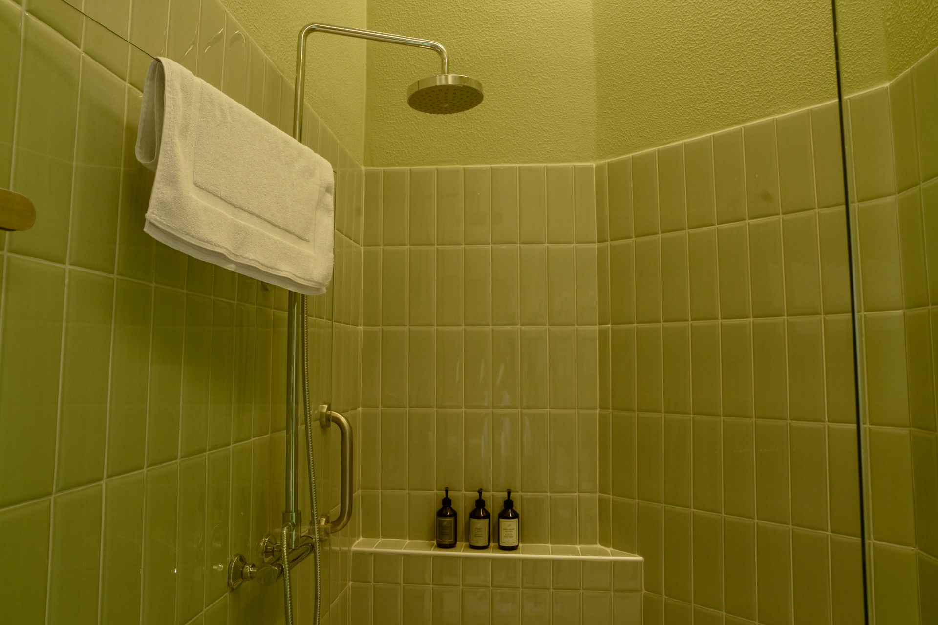 Un baño con azulejos verdes y una ducha con una toalla colgada en la pared.