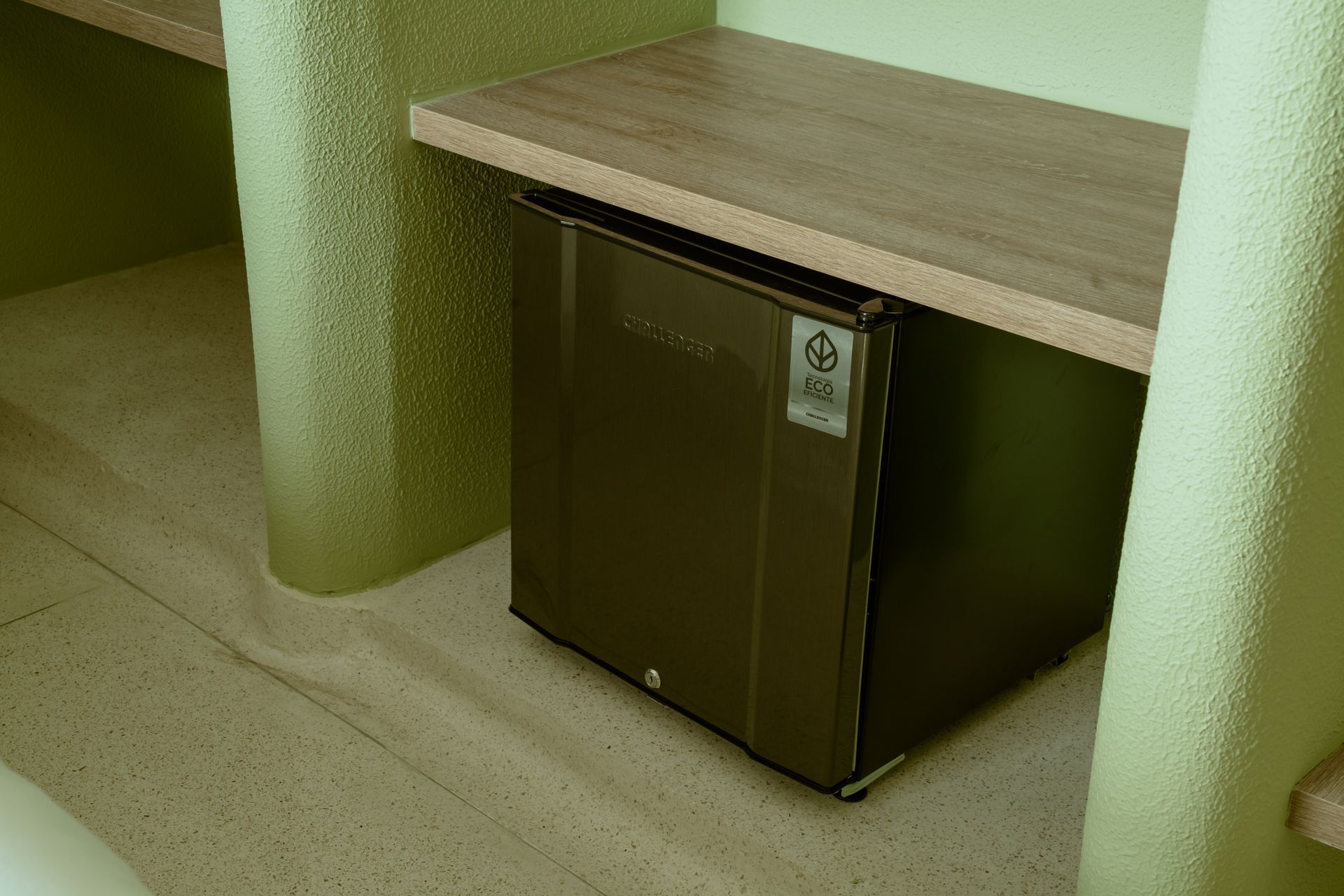 Un pequeño refrigerador está ubicado debajo de un estante de madera en una habitación.