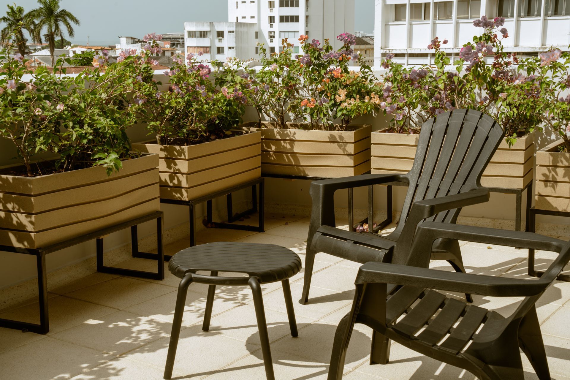 Dos sillas y una mesa en un balcón con jardineras al fondo.