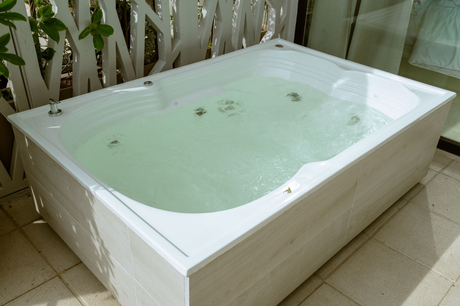 Una bañera blanca llena de agua verde está sobre un suelo de baldosas.