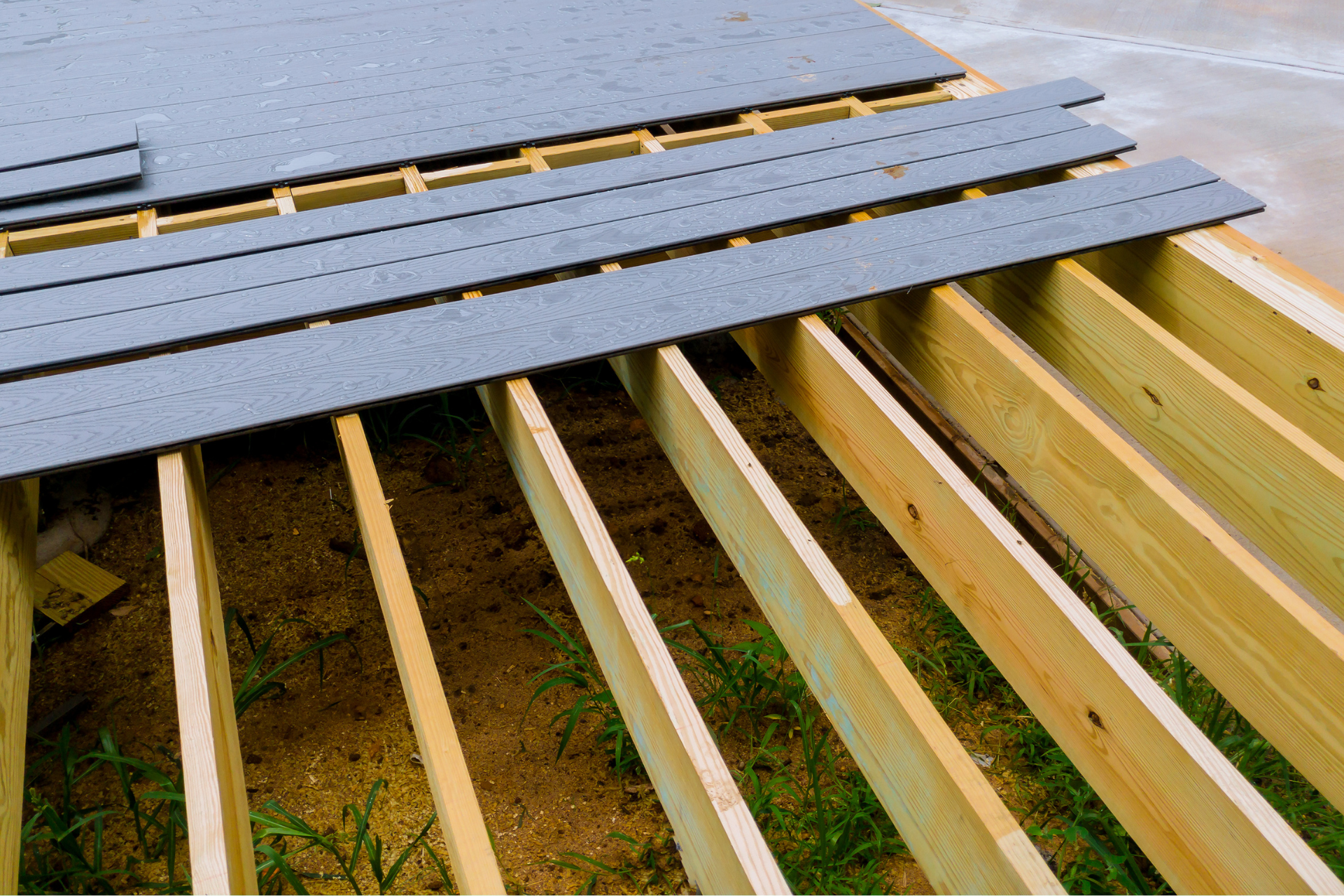 A photo of a deck in the process of being built. The deck has pressure-treated wood for the frame and grey composite deck boards for the flooring of the deck.