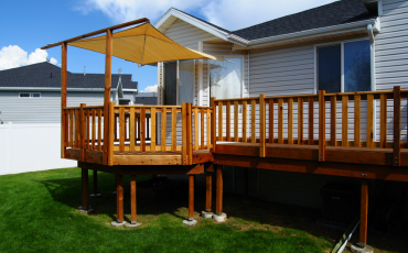 A photo of a deck with a portion of it covered to protect people from the sun. The other portion is un covered for people to enjoy the sun. It is an elevated deck with a railing around it to protect anyone from falling.