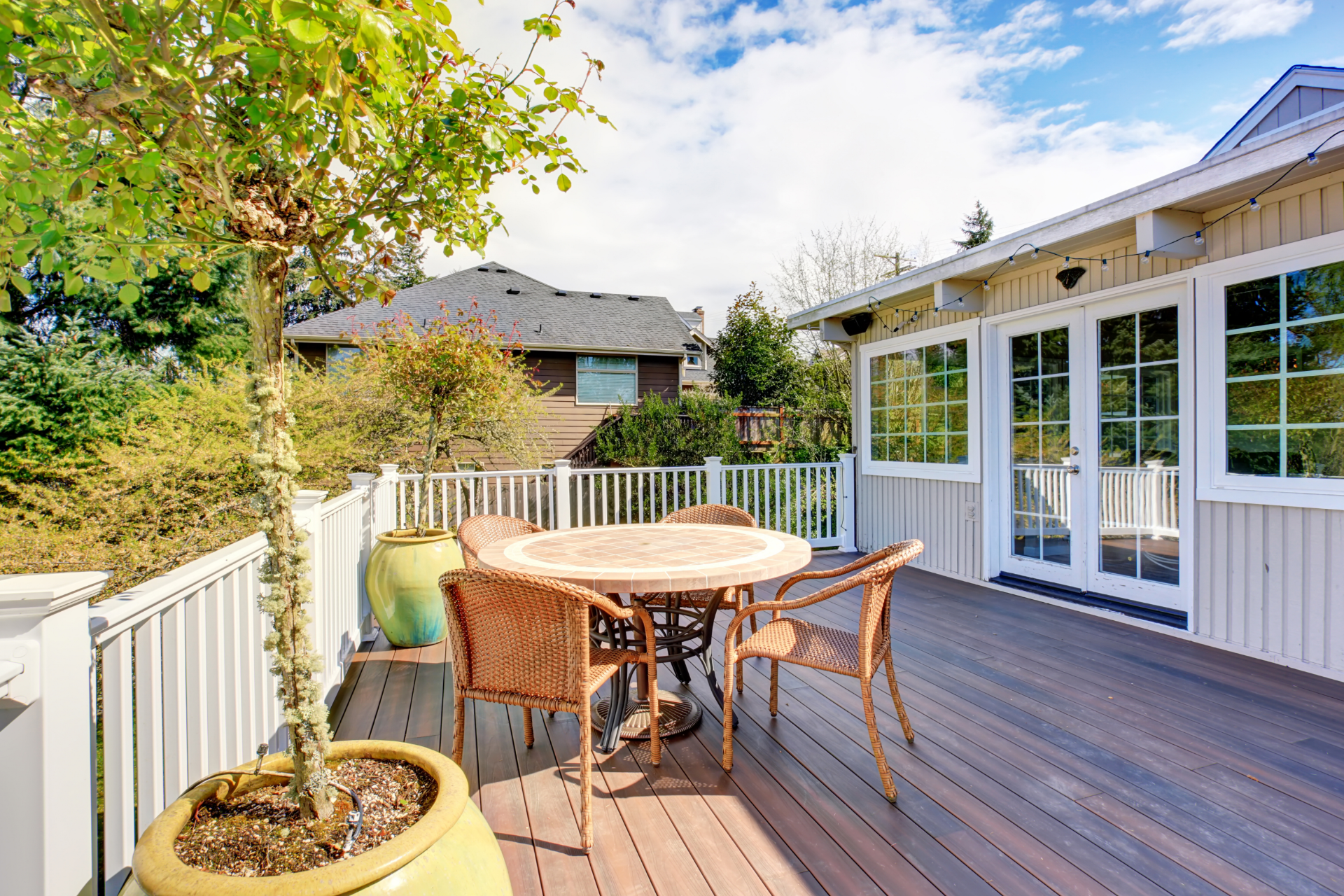 A photo of a house's backyard in Saint Paul, Minnesota. Most of the backyard space is taken up by their deck. There are two large pots with trees on the deck and a table with four chairs. It is a beautiful day in the photo with the sun shining and only a few clouds in the sky