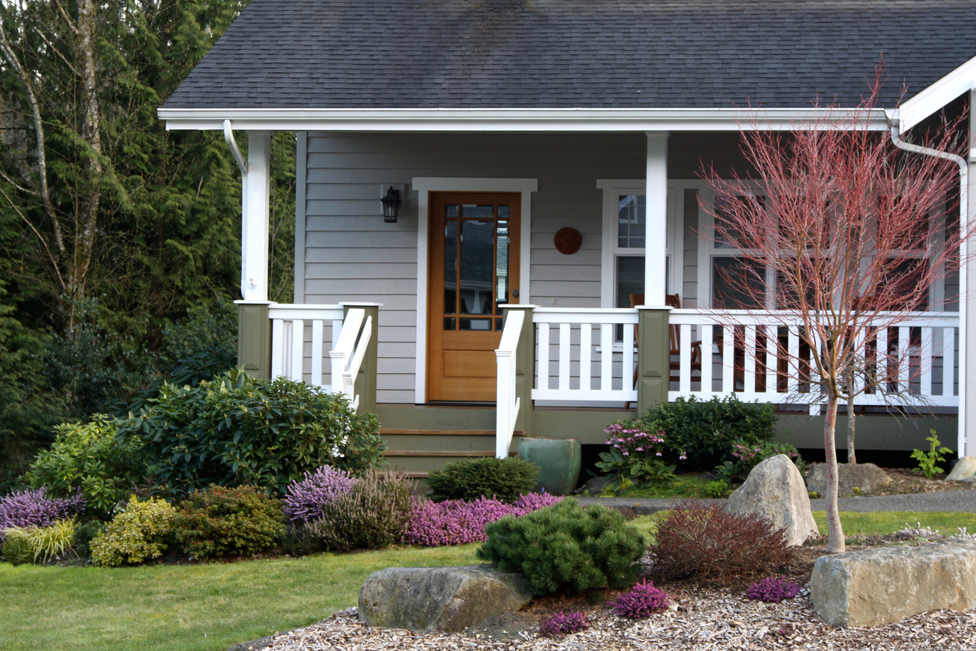 A photo of the front of a house in St Paul, Minnesota. The front of the house has a small yet beautiful porch. The porch has a railing around the perimeter and lots of plants and flowers in the flower bed in front of the house.