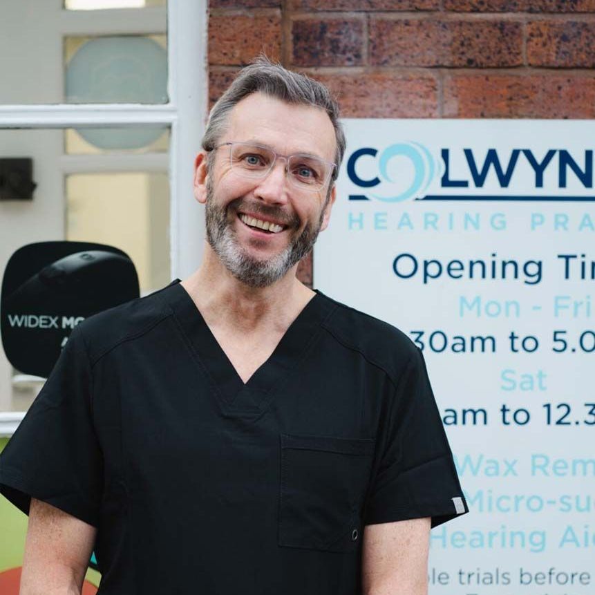 A man standing in front of a colwyn hearing practice sign