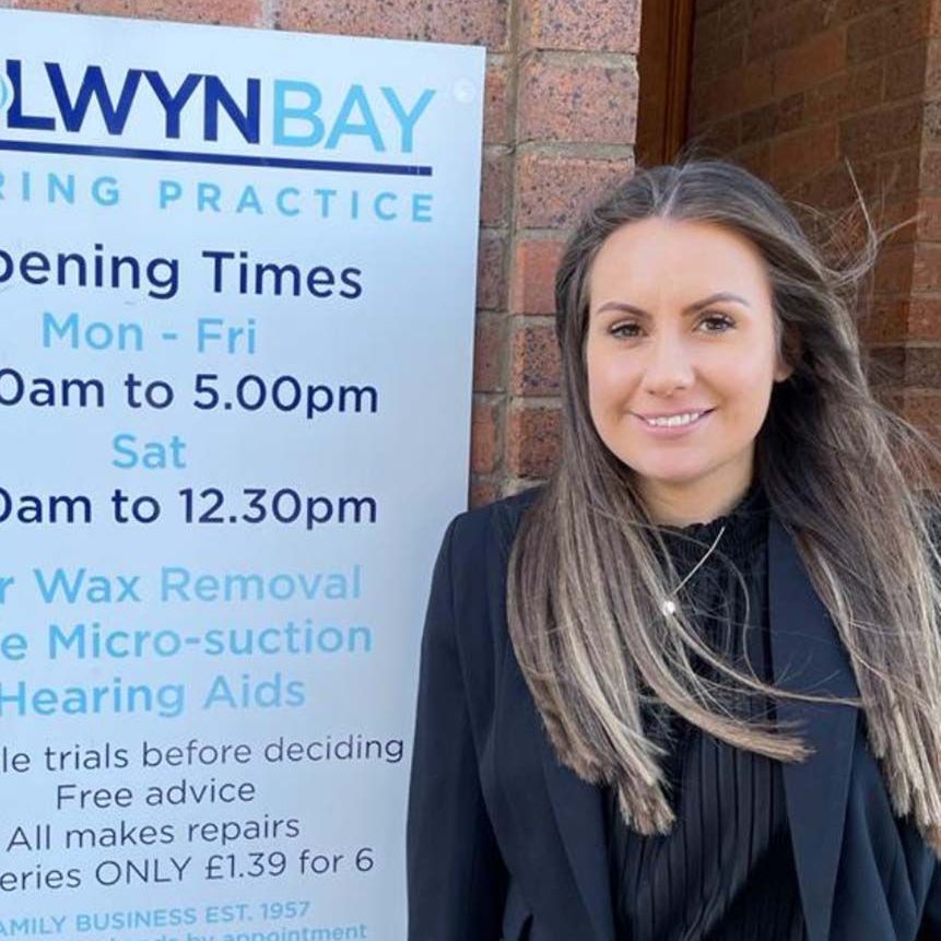 A woman is standing in front of a sign for lwynbay hearing practice