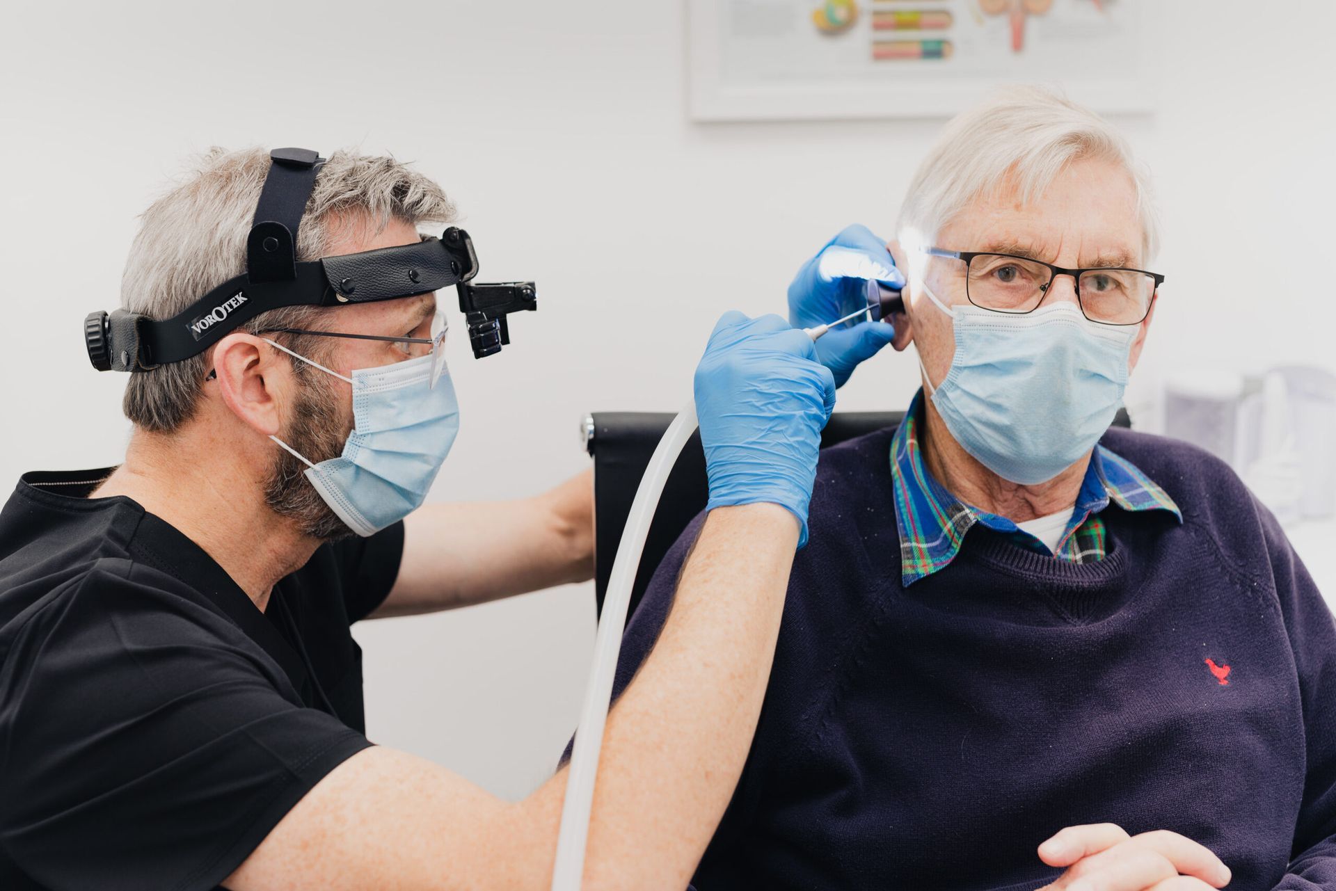 A man wearing a mask is getting his ear examined by a doctor.