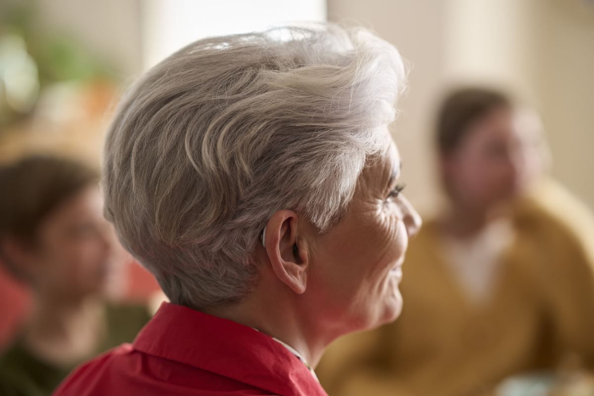 A woman with gray hair is wearing a hearing aid and smiling.