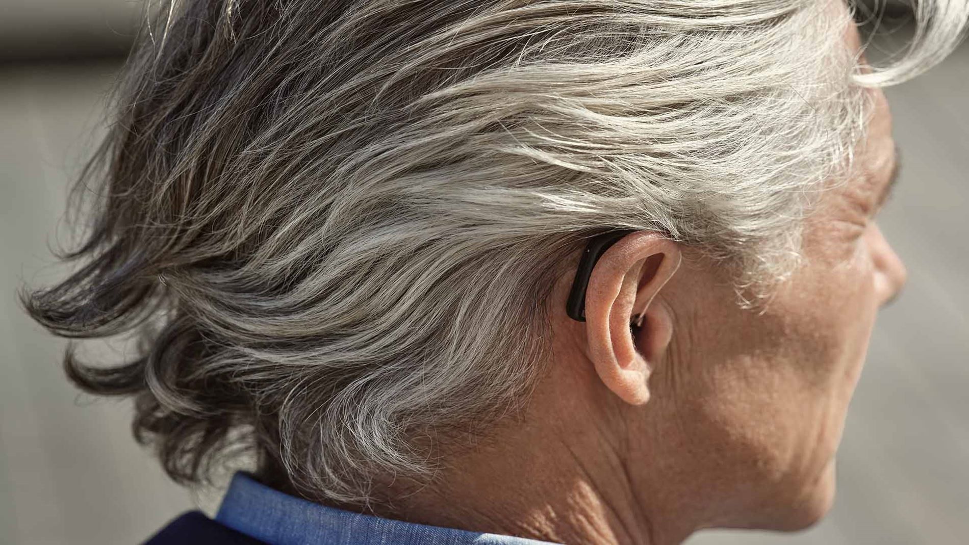 A man with gray hair is wearing a hearing aid.