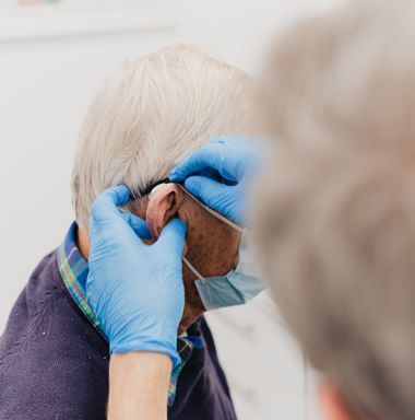 A man wearing a mask and gloves is getting his ears examined by a doctor.