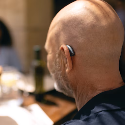 A bald man wearing a hearing aid in his left ear