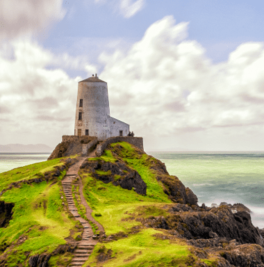 A lighthouse on top of a grassy hill overlooking the ocean.