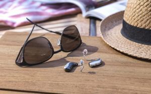 A pair of hearing aids and sunglasses are sitting on a wooden table next to a hat.