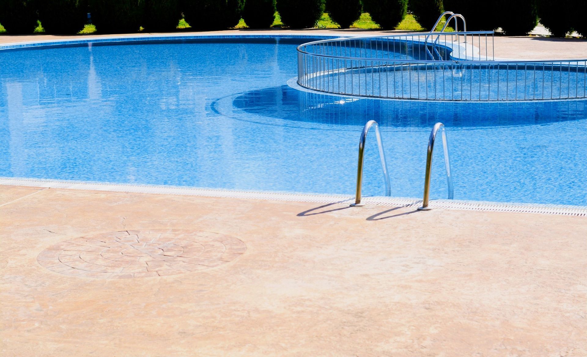 Clean pool with metal ladder and custom concrete deck on a sunny day