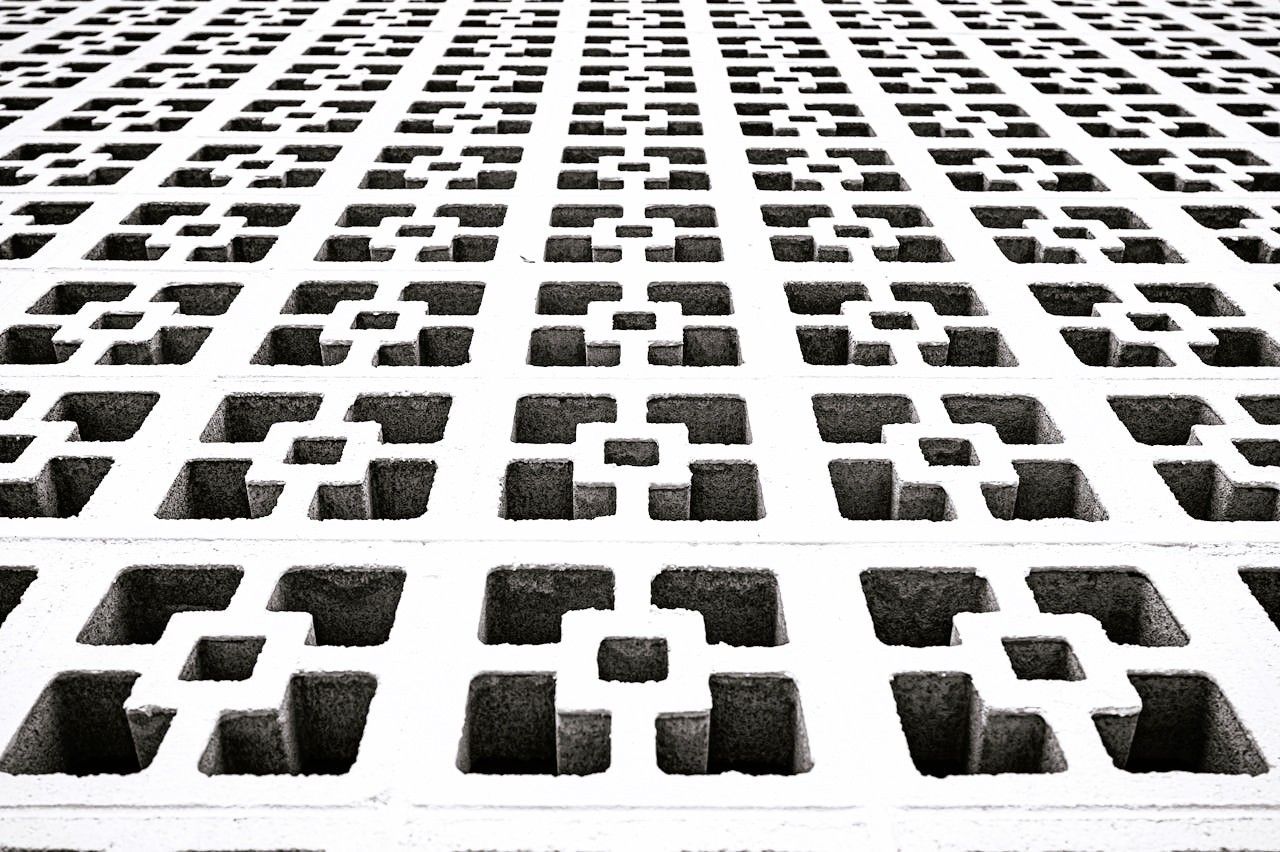 A textured facade of decorative concrete with a geometric pattern of square holes in a white wall