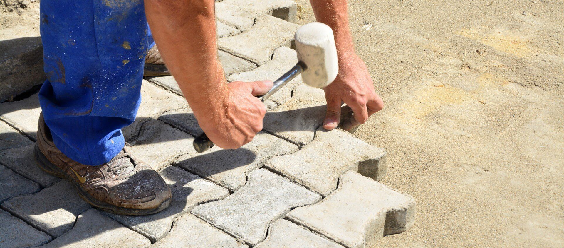 Man installing his DIY concrete pavers and hammering them to keep them in place