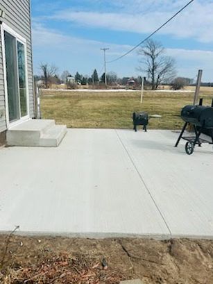 A concrete patio with a grill on it in front of a house.