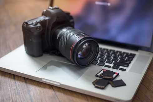 Camera with lens on laptop keyboard; SD cards nearby, on a wooden surface.