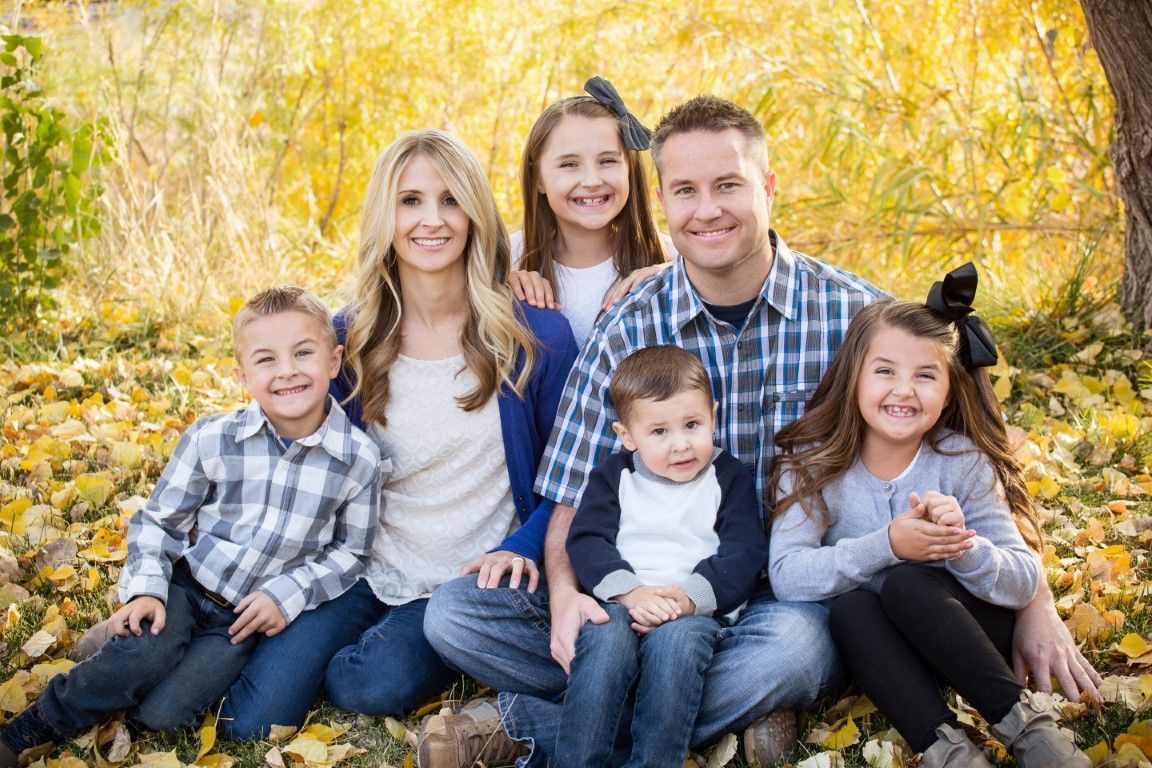 Family of six smiling, seated amongst fall foliage.