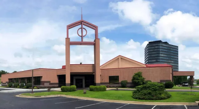 Rendering of a memorial with a central cross and surrounding structures, trees, and sky.