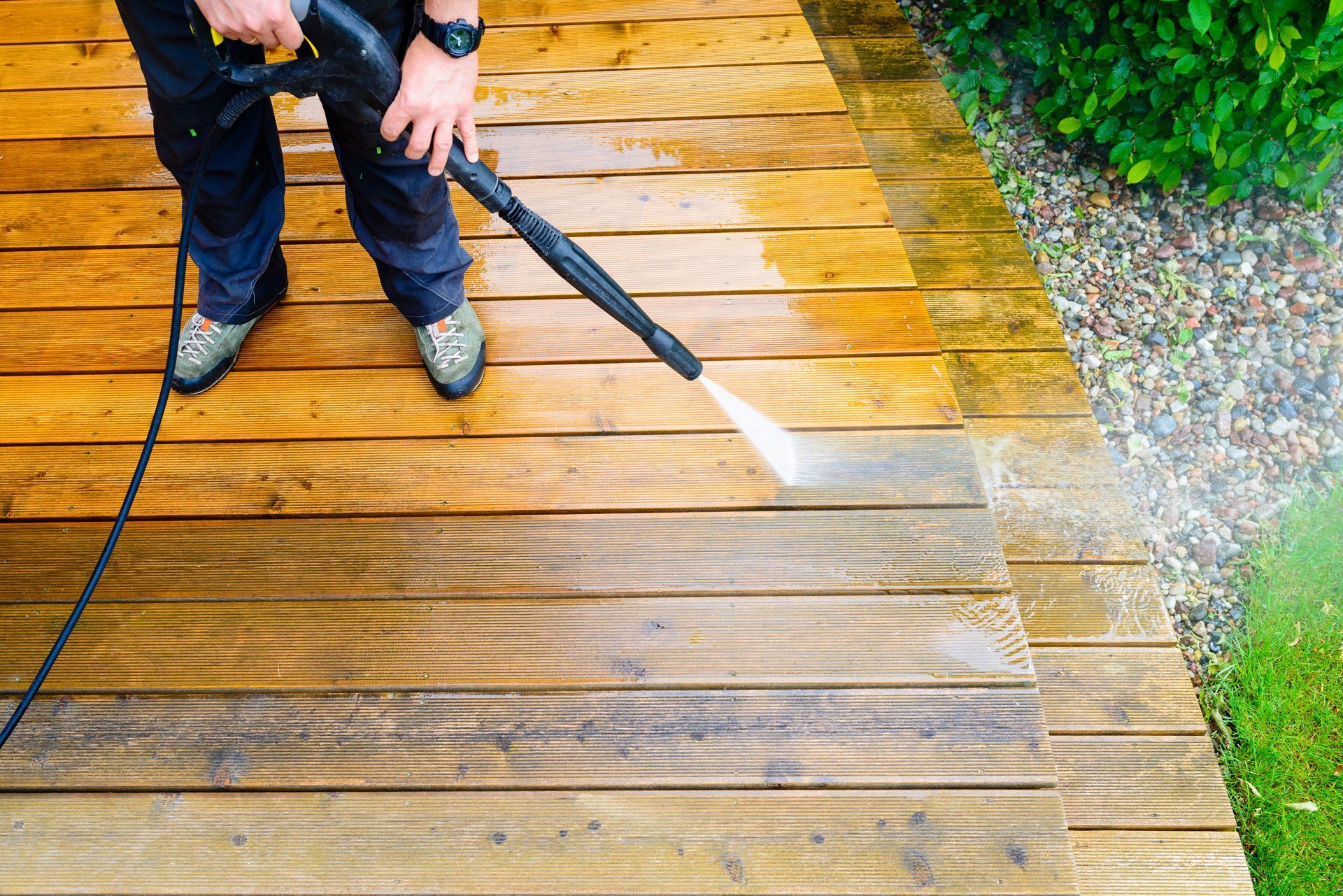 A man is using a high pressure washer to clean a wooden deck.