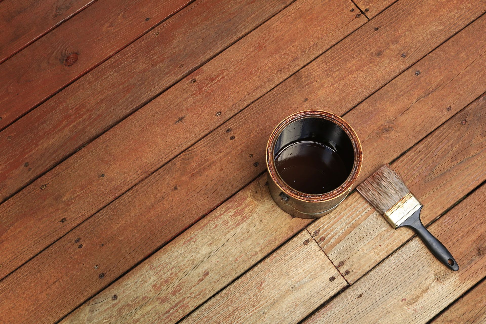 A bucket of paint and a brush on a wooden deck.