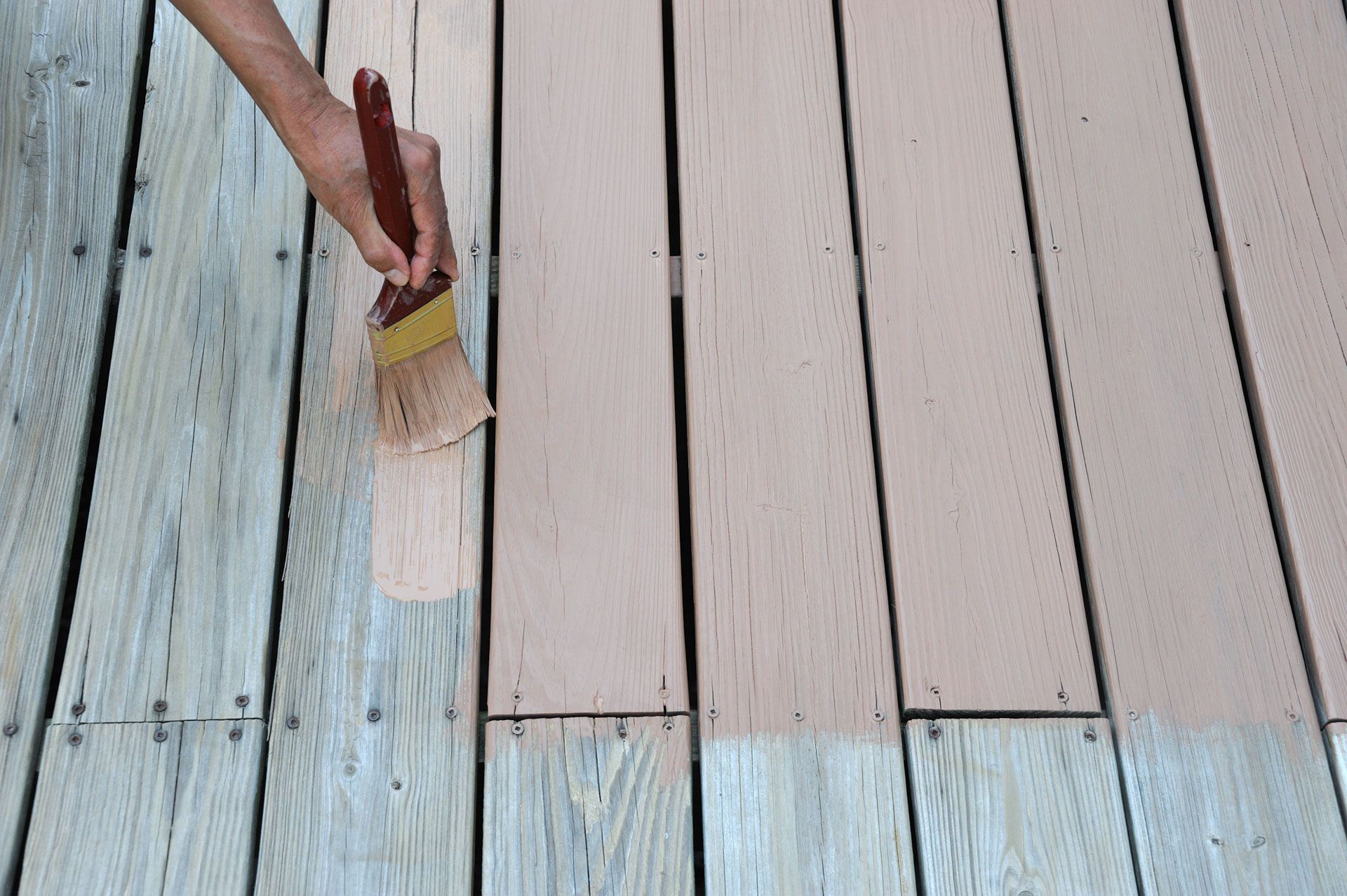 A person is painting a wooden deck with a brush.