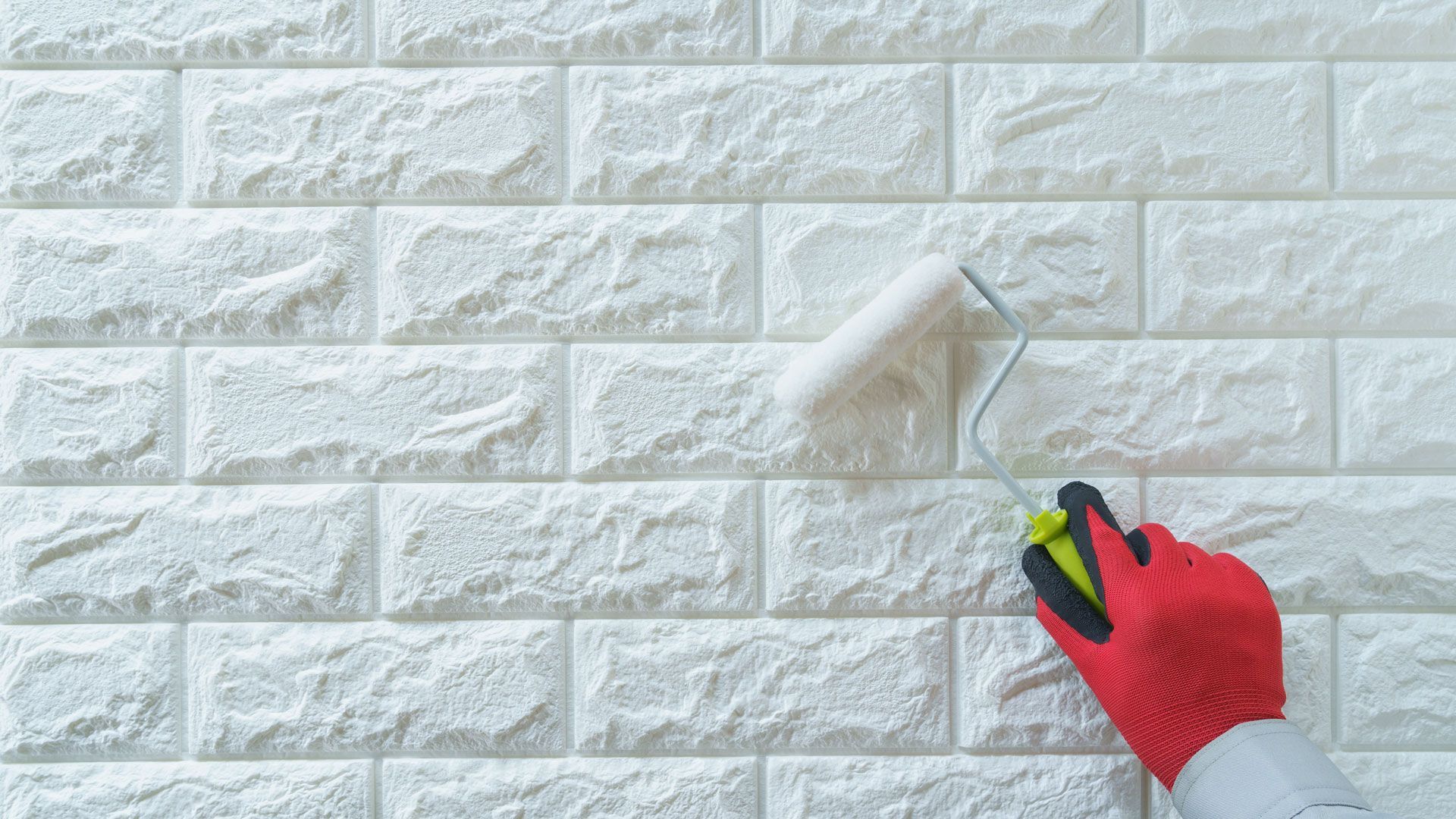 A person is painting a white brick wall with a roller.