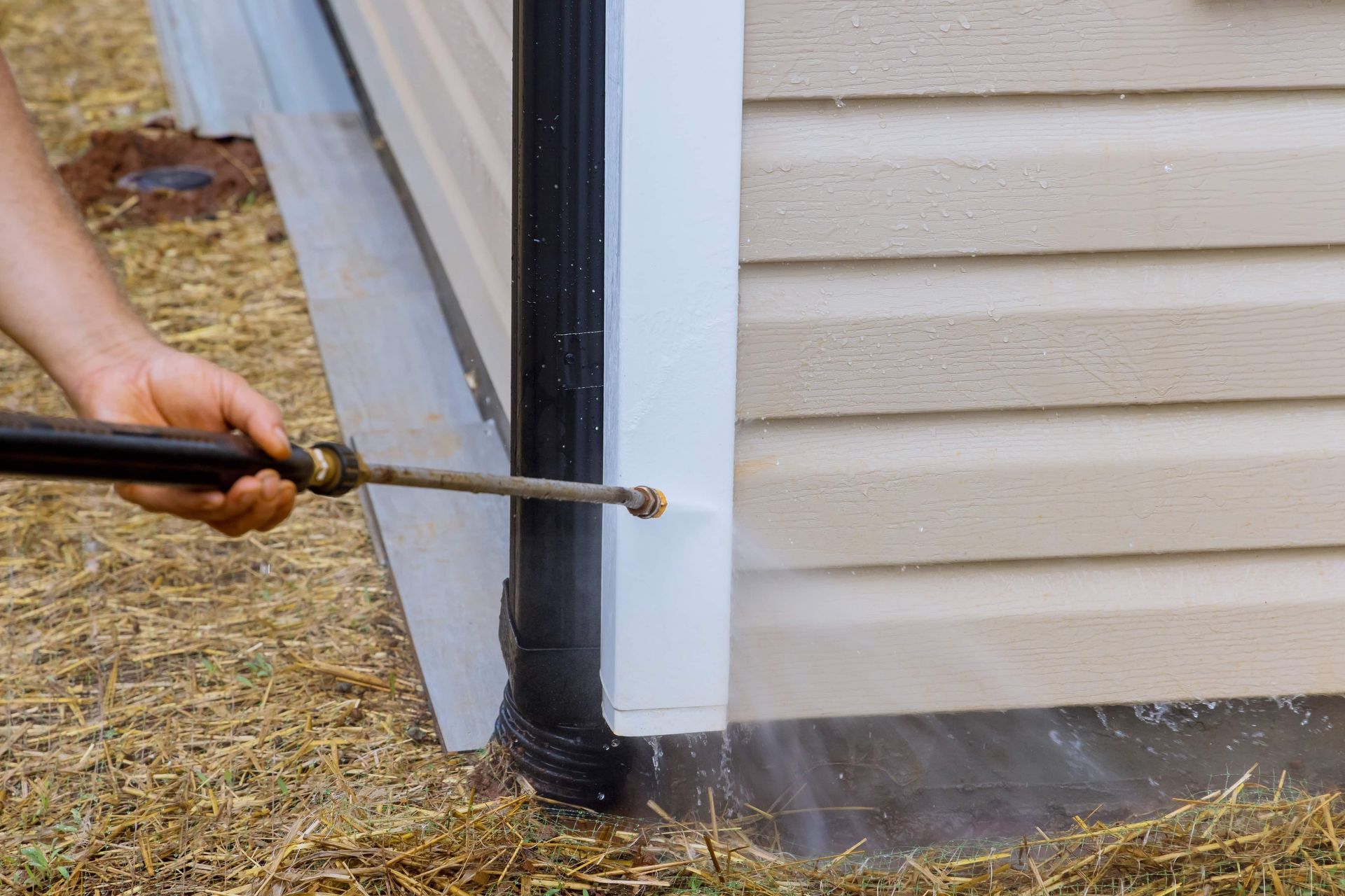 A person is cleaning the gutters of a house with a pressure washer.