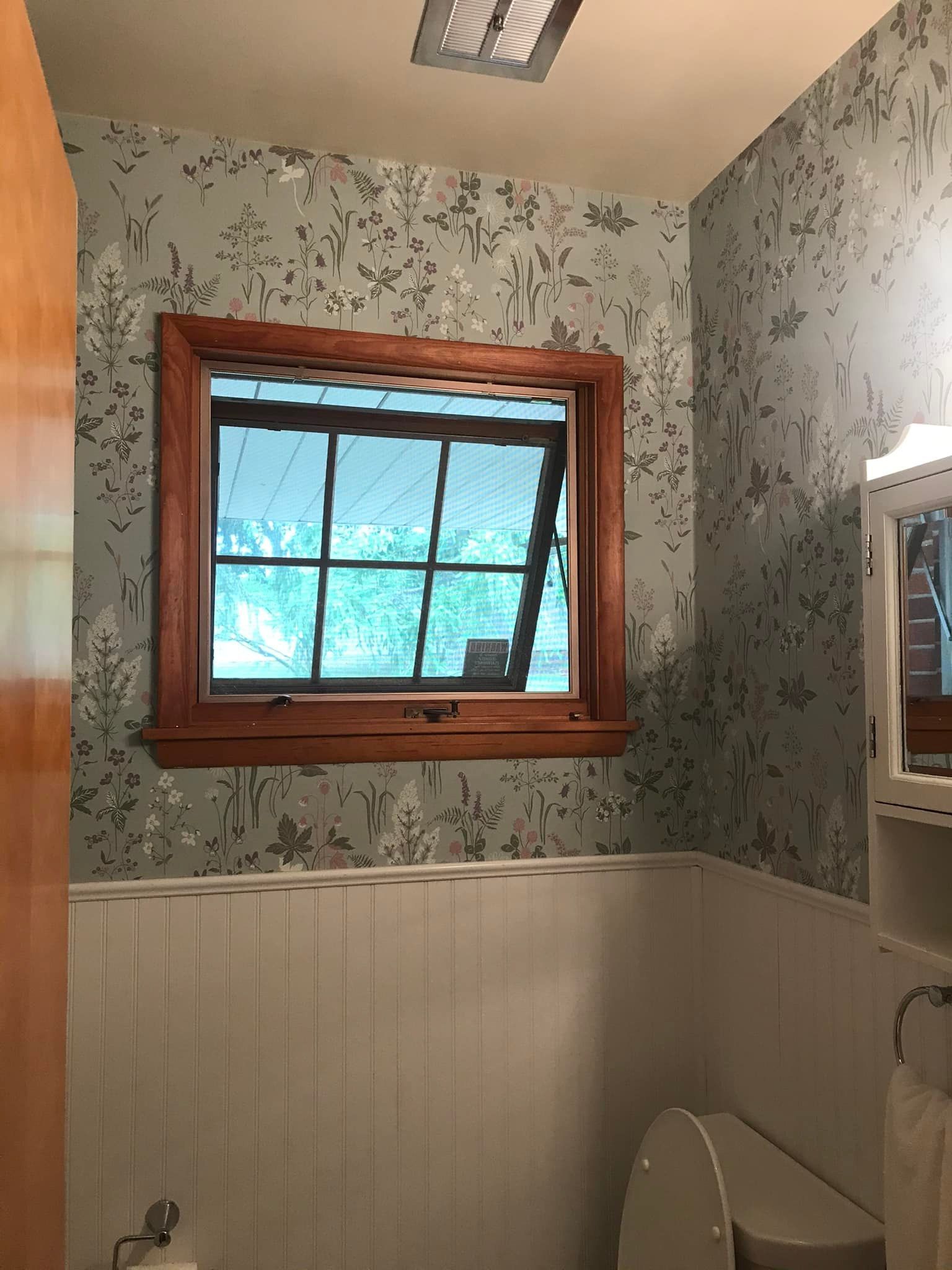 A bathroom with a toilet , sink , mirror and window.