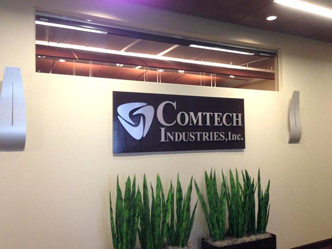 A sign for comtech industries inc. hangs on a wall.