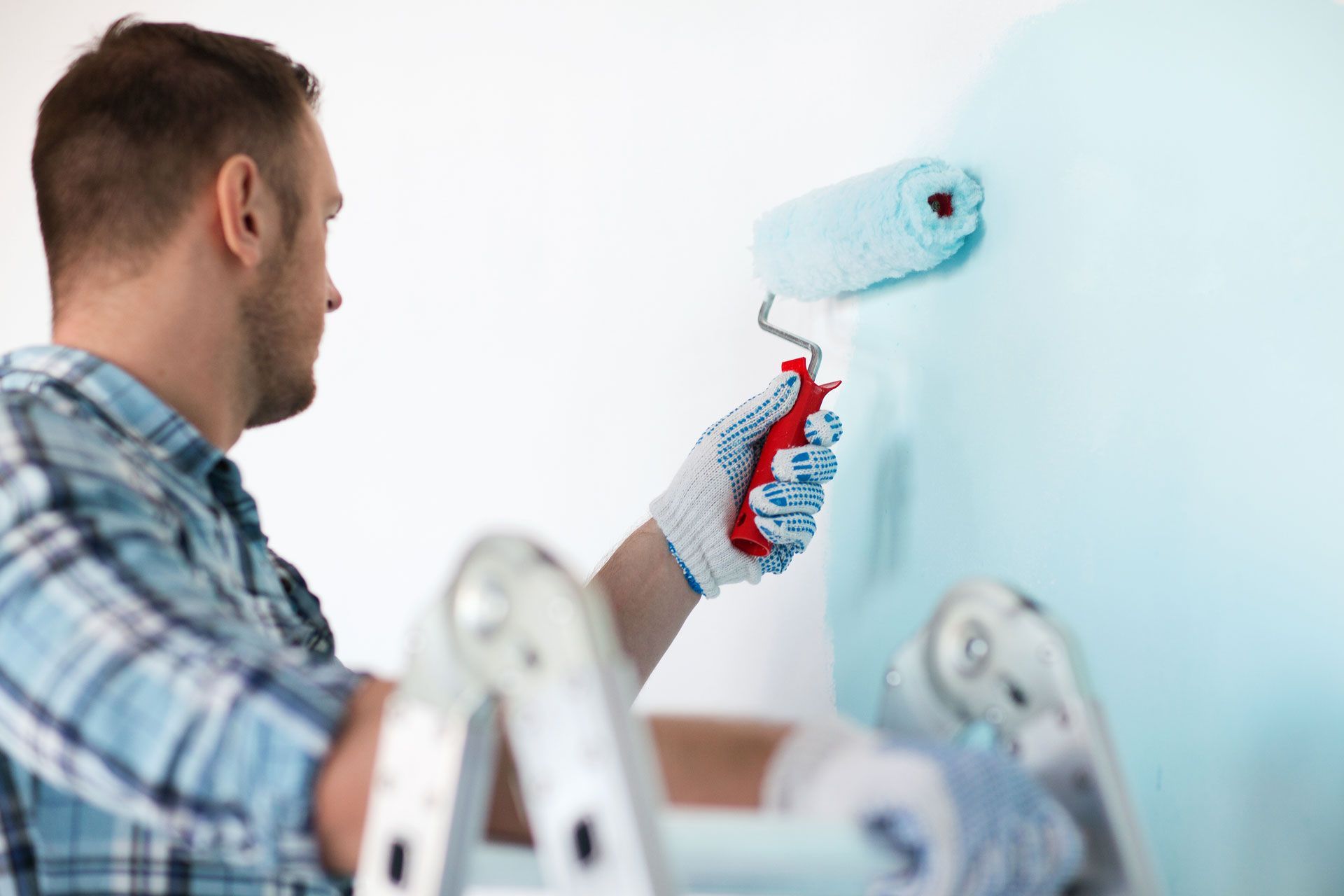 A man is painting a wall with a roller while standing on a ladder.