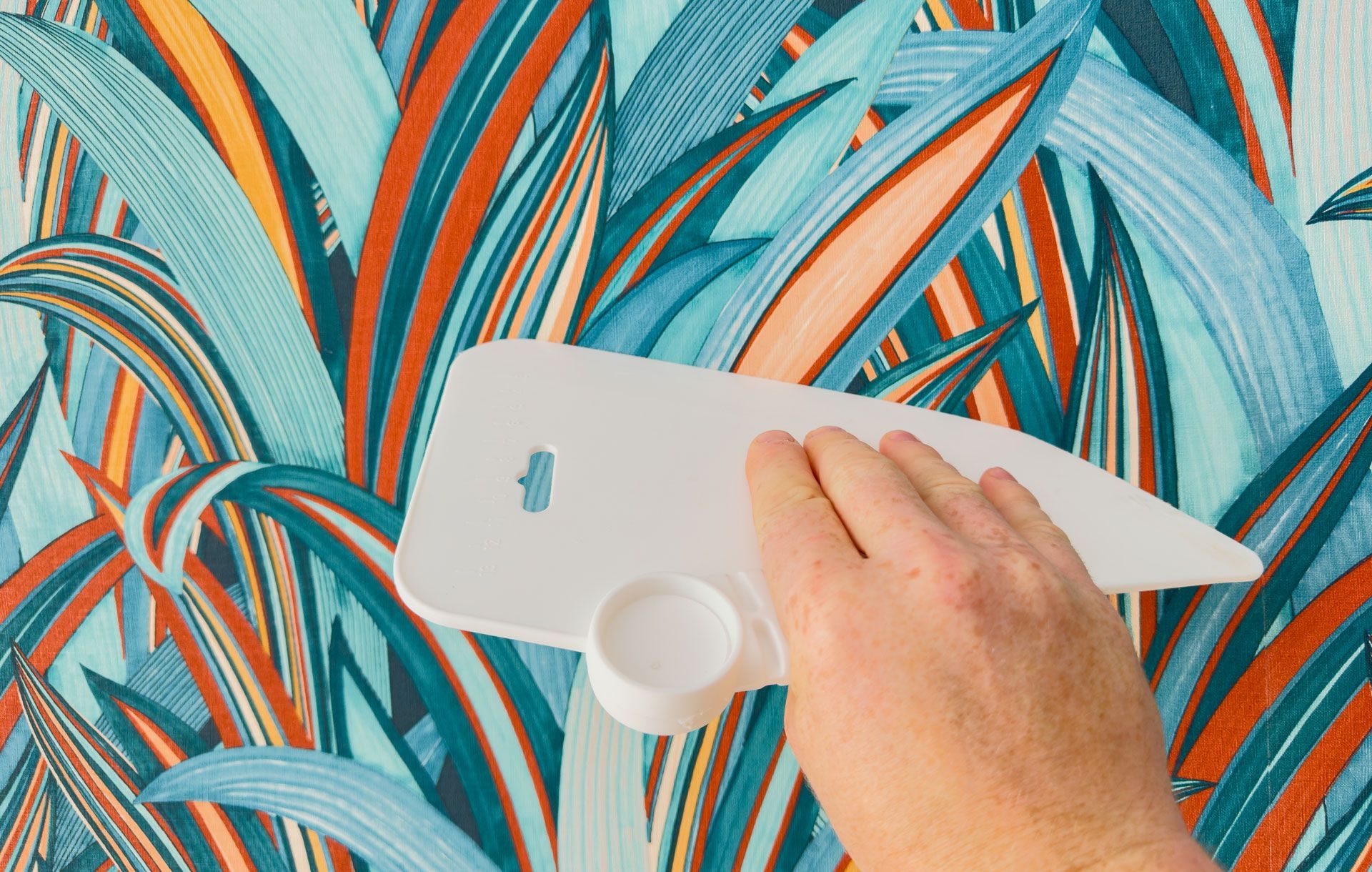 A person is applying wallpaper to a wall with a spatula.