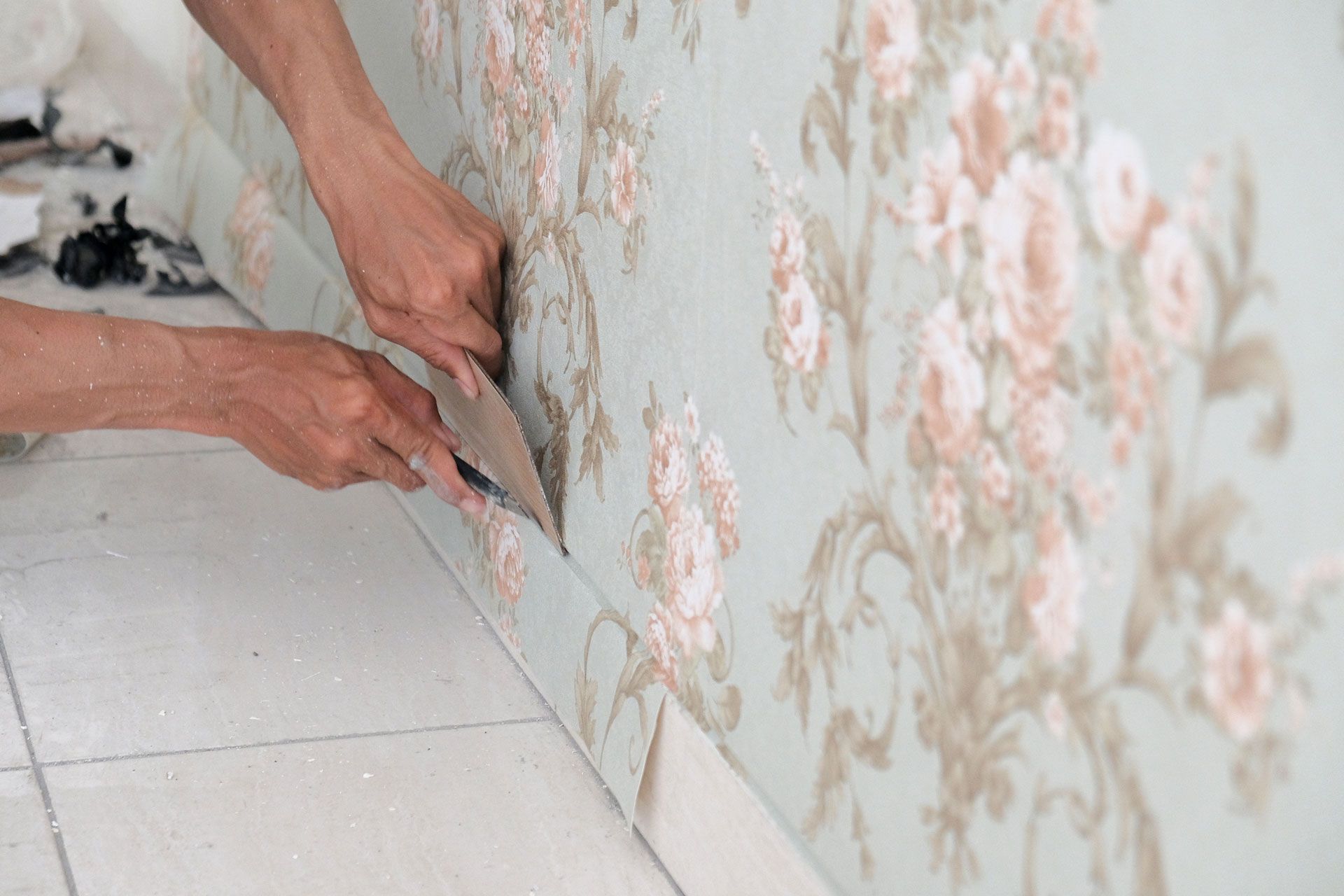 A person is removing wallpaper from a wall with a spatula.