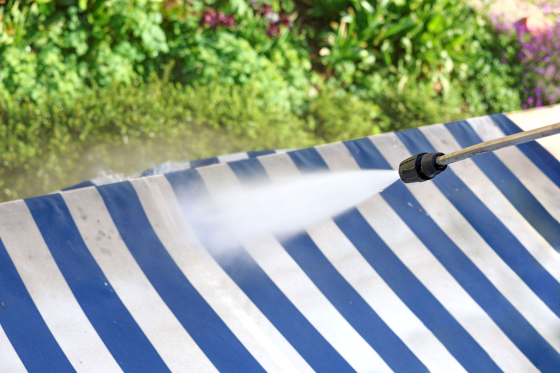 A person is cleaning a blue and white striped awning with a high pressure washer.